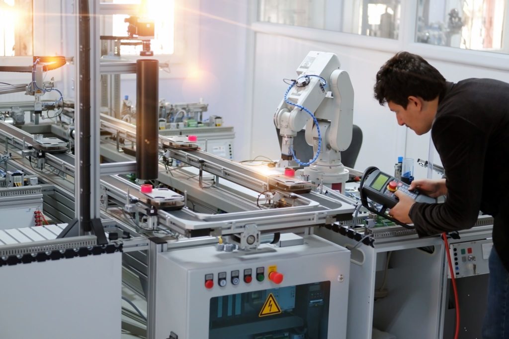 man working controls of robotic arm in industry 4.0 smart factory production line