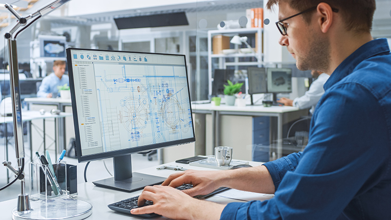 Over the shoulder shot of design engineer working with CAD software on desktop computer, Screen shows medical device manufacturing technical drafts and drawings.