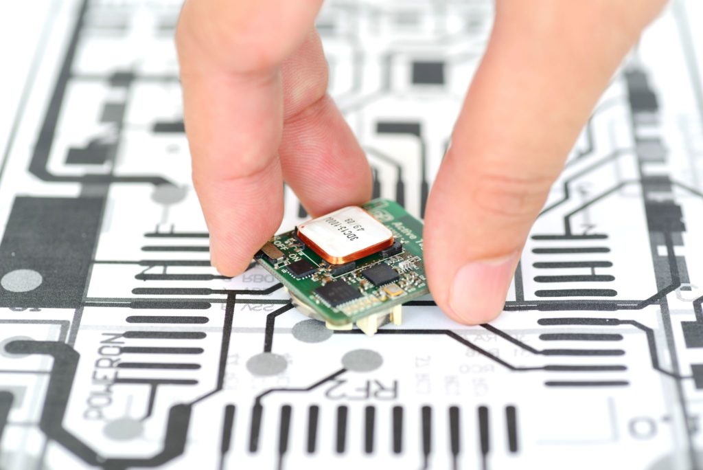 Closeup of hand picking up a PCBA on a schematics background