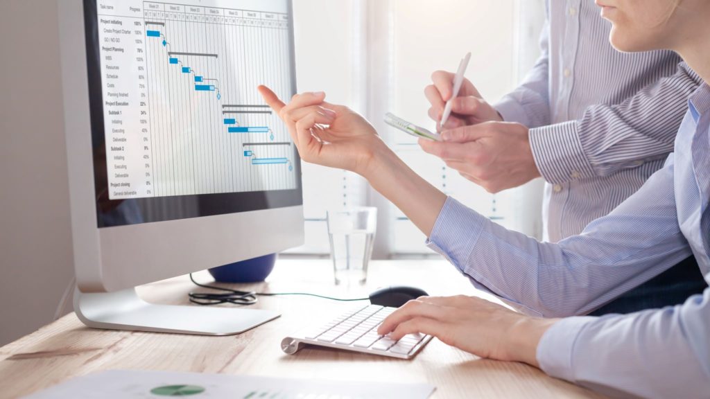 Project management team updating planning schedule with Gantt chart open on computer.