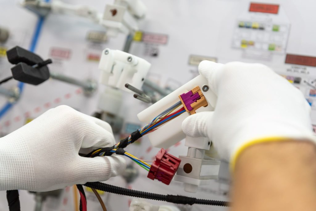 Closeup of gloved technicians hands checking a cable harness assembly.