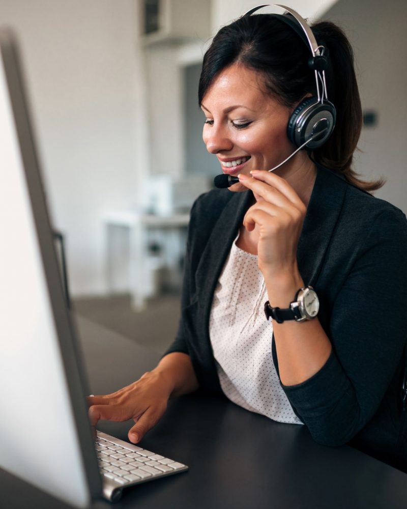 Female customer service representative working on a computer while talking to a client via a headset.