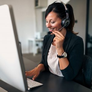 Female customer service representative working on a computer while talking to a client via a headset.